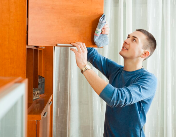 A man cleaning brown kitchen cabinets